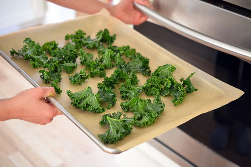 Someone putting a tray of kale into the oven for kale chips.