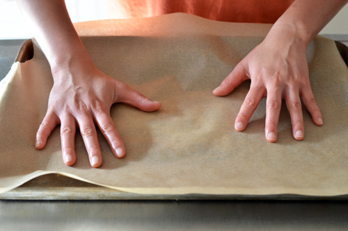 Someone lining a baking tray with parchment paper.