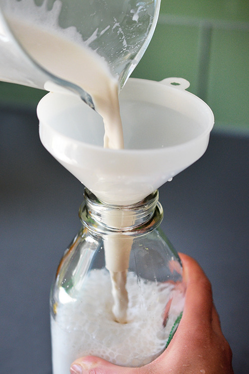 Pouring the vanilla almond milk mixture into a glass bottle.