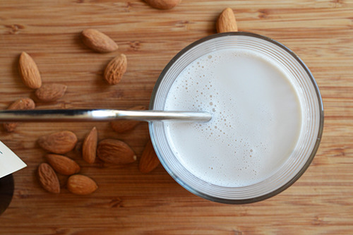 A cup of homemade paleo vanilla almond milk on a cutting board with raw almonds scattered around it.