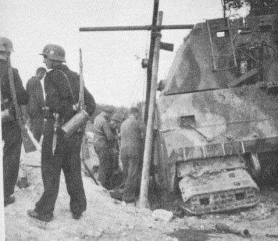 Soldiers standing around as technicians work on repairing the Maus prototype’s tracks and wheels.