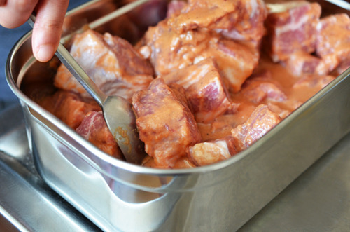 A spoon mixing the marinade and cubed pork shoulder so they are well-coated. 
