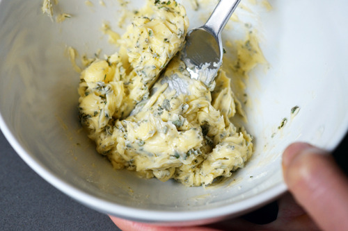 Mixing up the herb butter in a white bowl with a fork.
