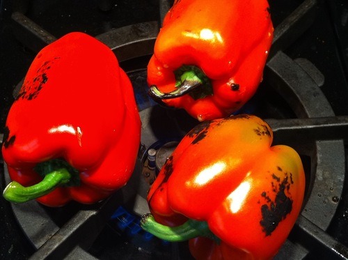 Three red bell peppers roasting directly on top of a gas range.