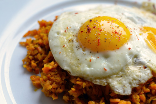 A close up shot of Sweet Potato Hash (with Fried Eggs) on a white plate.