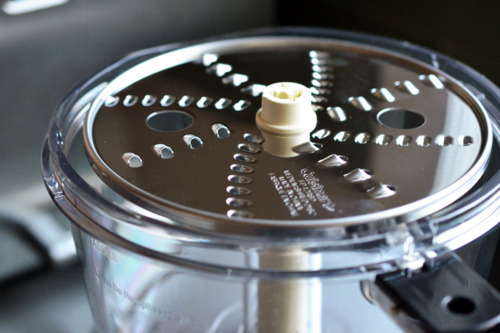 A closeup of a food processor fitted with a slicing blade.
