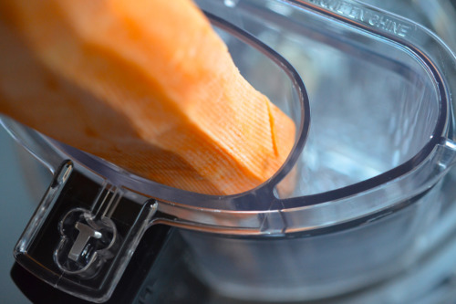 A peeled and cut sweet potato is inside the feeding tube of a food processor.