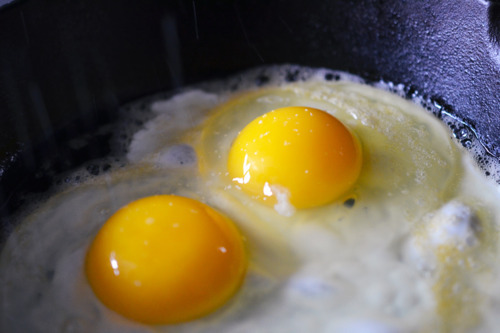 Two sunnyside up eggs frying in a small cast iron skillet