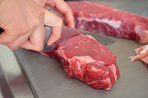 A New York boneless strip steak cut in half on a gray plastic cutting board.
