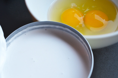 A bowl with two cracked eggs next to a can of full-fat coconut milk.