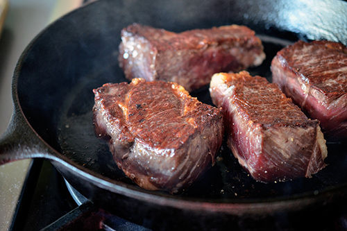 A shot of perfect steaks searing in a cast iron skillet with golden brown exteriors.
