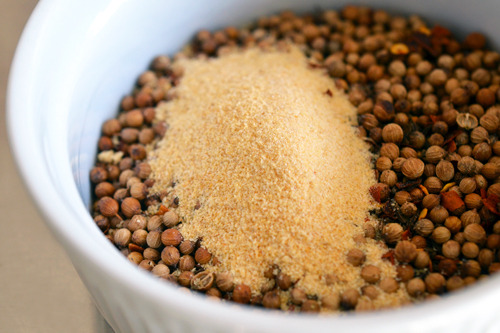 A spoonful of garlic powder is added to the bowl of toasted spices for the tabil seasoning blend.
