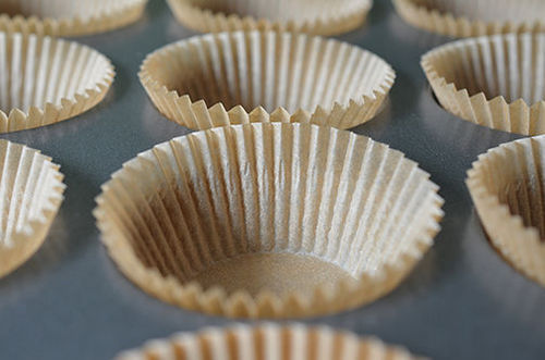 A side shot of a muffin tin lined with parchment paper liners 