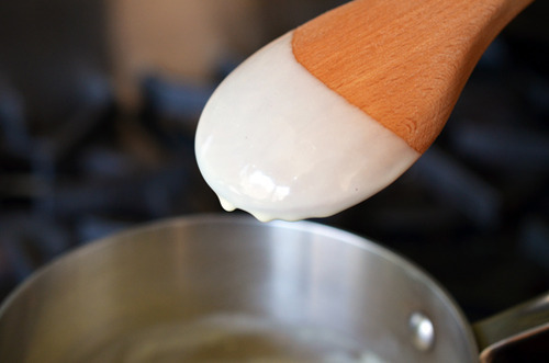 Thickened coconut milk dripping off a wooden spoon for Mexican chocolate pots de crème.