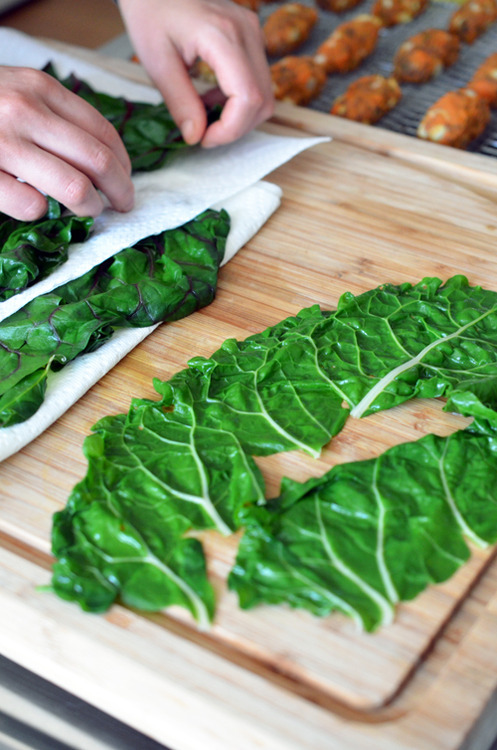 Someone rolling out the boiled swiss chard leaves onto paper towels to dry them.