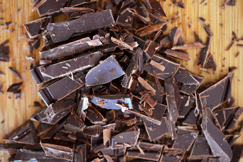 Thinly sliced dark chocolate on a cutting board for Grain-Free Dark Chocolate Cherry Scones.