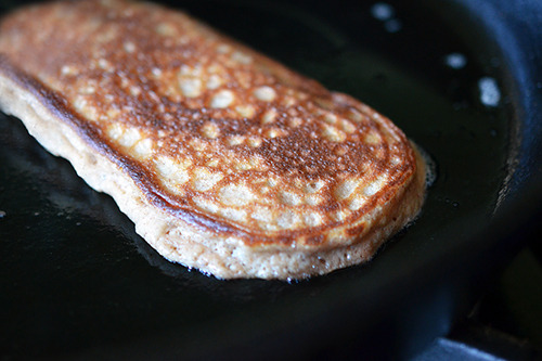 A paleo pancake is shown frying in a cast iron skillet.