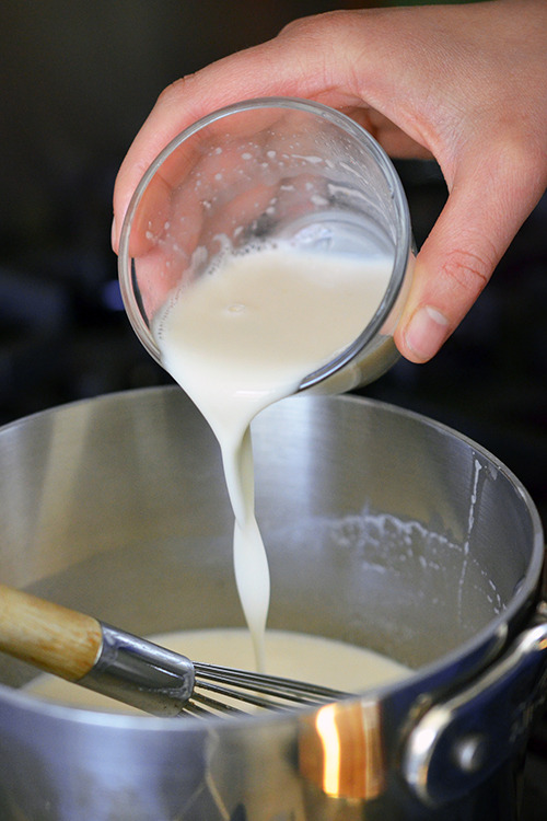 Pouring the gelatin mixture into the warmed milk mixture in a pot for panna cotta with strawberry balsamic compote.