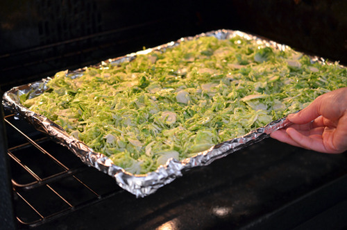Placing the baking sheet of shaved Brussels Sprouts into an oven. 