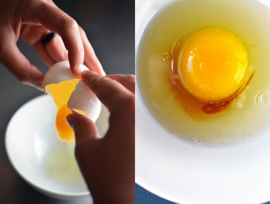 Someone cracking an egg into a white bowl with a few drops of fish sauce.