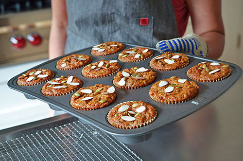 A person carrying a muffin tin filled with Paleo Pumpkin and Carrot Muffins 