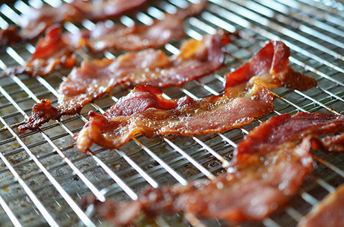 A side view of cooked bacon on a stainless steel wire rack.