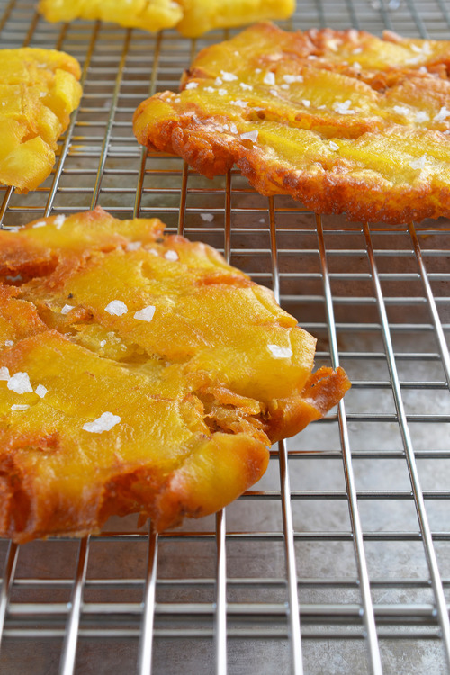 The paleo fried green plantains or patacones sitting on a cooling rack with salt on top.