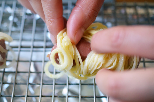 Two hands prying apart the spiralized sweet potatoes on a hotdog to expose the face on the Yummy Mummies 
