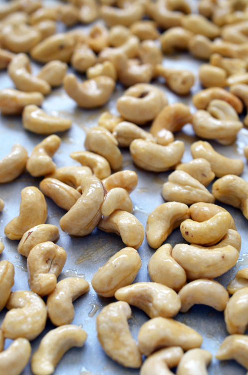 Honey vanilla cashews on a parchment covered tray ready to be baked.