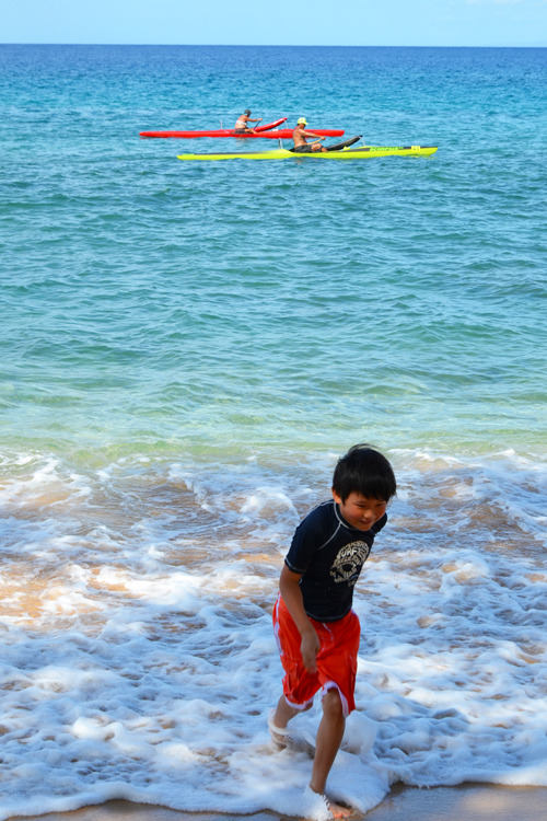 A smiling Asian boy walking out of the ocean onto the beach in Hawaii