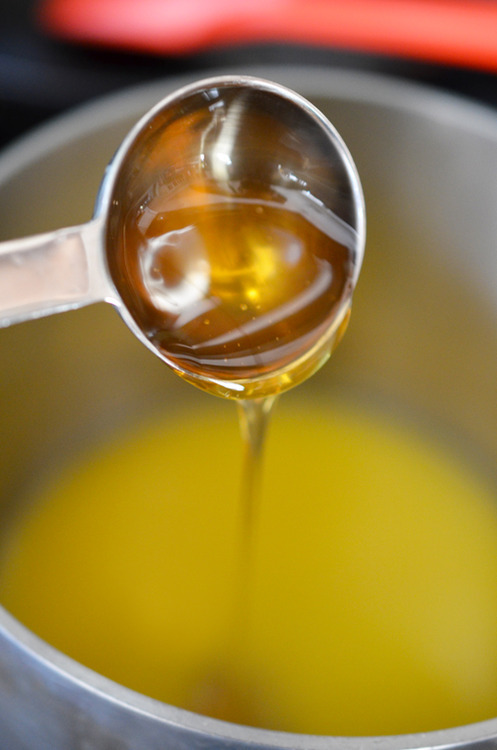 Honey in a measuring spoon is being poured into a pot with orange juice.