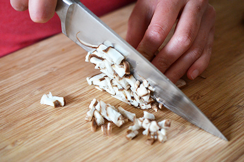 Mincing shiitake mushrooms on a wooden cutting board with a chef's knife.