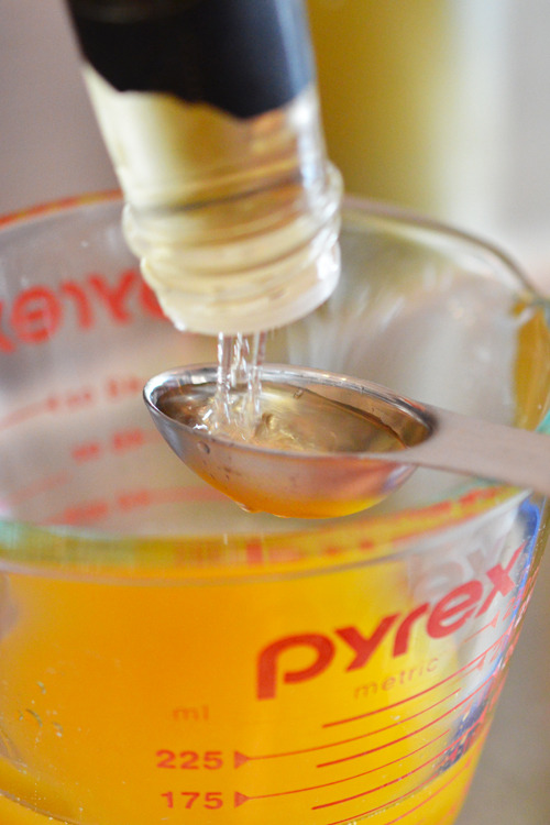 Pouring rice vinegar into a measuring spoon above a measuring cup filled with orange juice.
