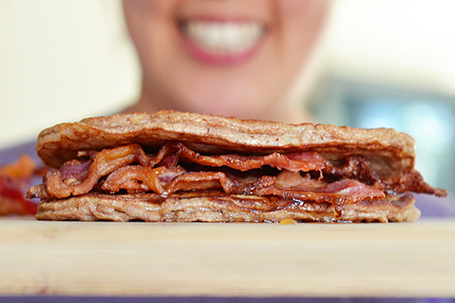 A side view of a Bacon Pancake Sandwich with someone smiling in the background.