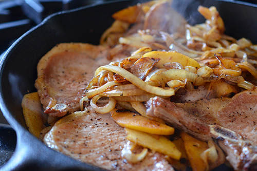 The seared pork chops in the cast iron skillet with the sautéed onions and apples.