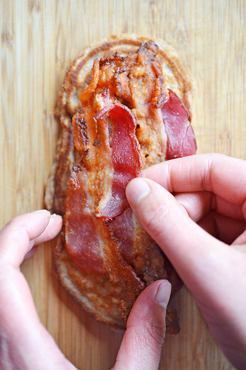Cooked bacon is being placed on a Bacon Pancake Sandwich.