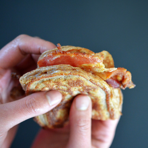 Two hands holding a Bacon Pancake Sandwich.