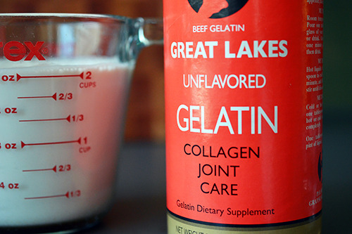 A closeup of a bottle of unflavored gelatin next to a measuring cup of almond milk.