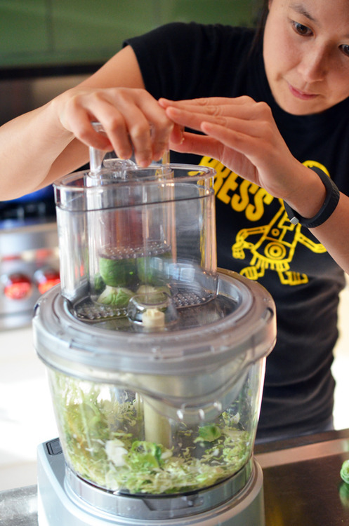 A woman using a food processor to shred Brussels Sprouts for Warm Brussels Sprouts Slaw with Asian Citrus Dressing 