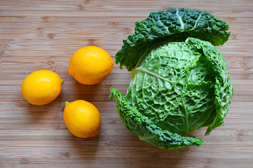 Three lemons and a cabbage on a cutting board.