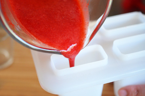 Pouring the strawberry purée mixture into the bottom of the ice pop trays.