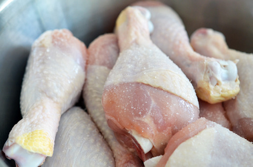 Salting raw chicken legs in a large bowl.