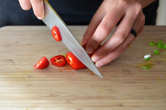 Slicing a red jalapeno pepper on a wooden cutting board.