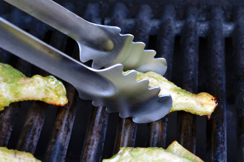 A tong grabbing onto a chili lime chicken wing on a grill.