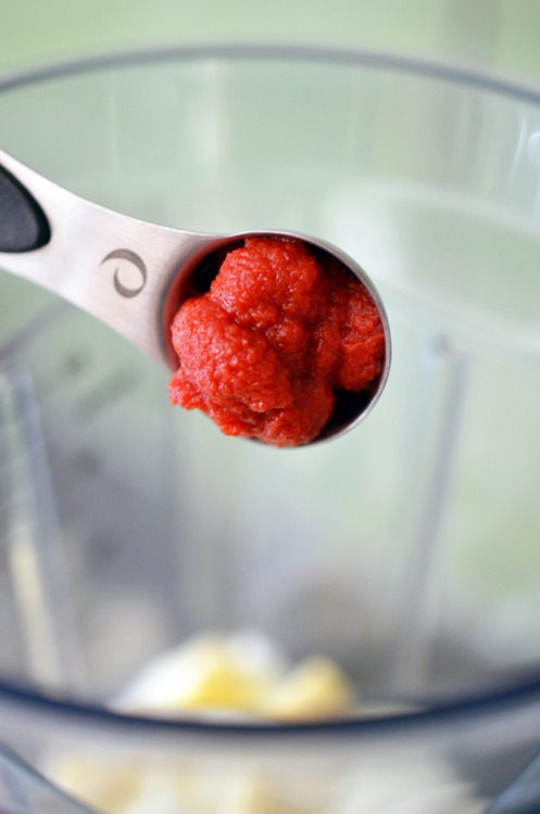 Sriracha in a measuring spoon being poured into a blender.