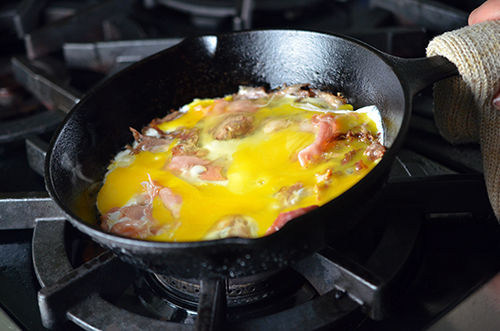 A small cast iron pan cooking the eggs and prosciutto for Pig in a Skillet.