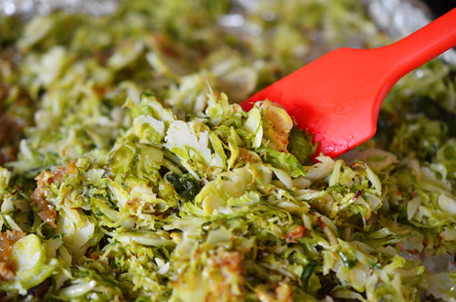 A red silicone spatula is tossing Warm Brussels Sprouts Slaw with Asian Citrus Dressing on a rimmed baking sheet.
