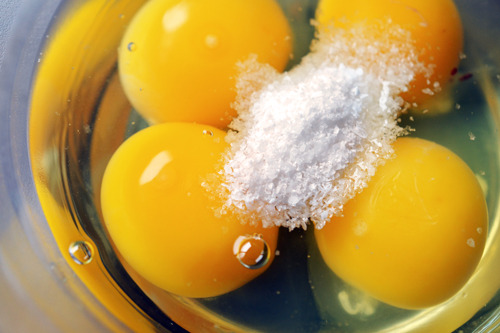 Four cracked and raw eggs in a bowl with salt.