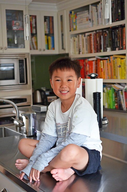 A young Asian boy is sitting cross-legged on a kitchen counter.