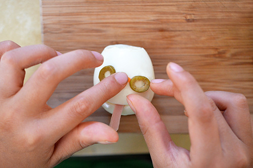 Someone putting olives on a hard boiled egg to mimic eyes for crazy clown eggs.